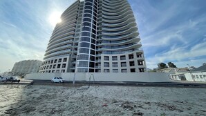 A modern multi-story building with a curved facade, large windows, and a flat roof. - Luxury Beachfront Apartment with Panoramic Ocean Views – Strand Ocean View 1004 (Strand)