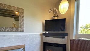 Een moderne woonkamer met een open haard, een flatscreen televisie, een decoratieve spiegel en een rieten fauteuil.