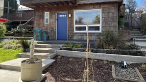 Een houten huis met twee verdiepingen, een blauwe deur, een balkon en een tuin met planten en een klein vijvertje.