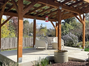 A covered patio with a wooden ceiling, outdoor seating, and a planter with a plant.