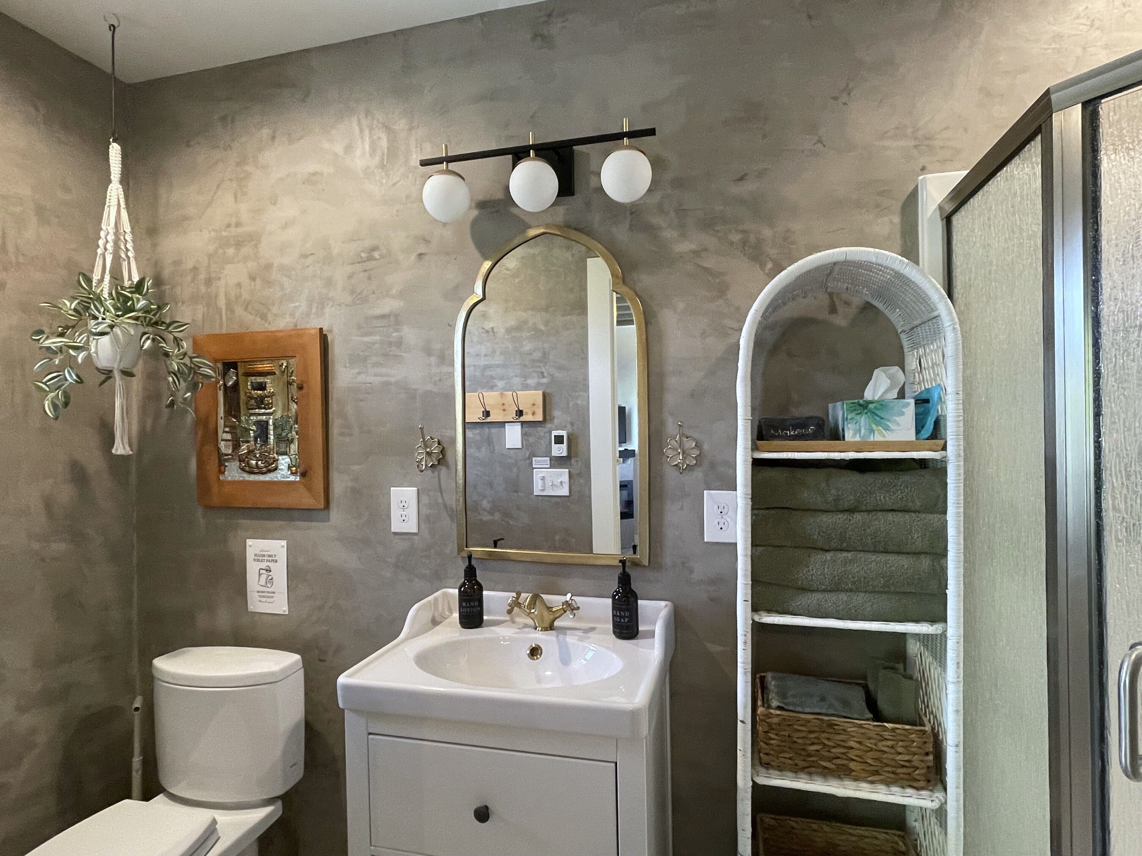 A bathroom with a white sink, a mirror, a hanging plant, and a shelf with toiletries.