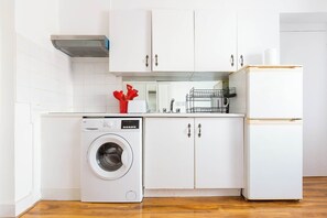 A compact kitchen with a washing machine, a refrigerator, and white cabinets. - Cosy 1BDR Studio Flat Perfect for Exploring London (Greater London)
