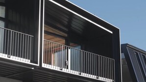 Ein modernes Gebäude mit einem Balkon, der weiße Geländer und eine Glastür hat.