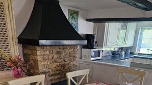 Uma sala de jantar com uma mesa posta para quatro pessoas, uma lareira de pedra e uma cozinha ao fundo.
