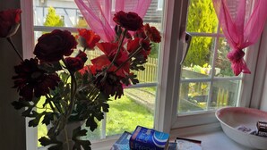 Uma janela com cortinas cor-de-rosa, um vaso com flores vermelhas e uma tigela no parapeito.
