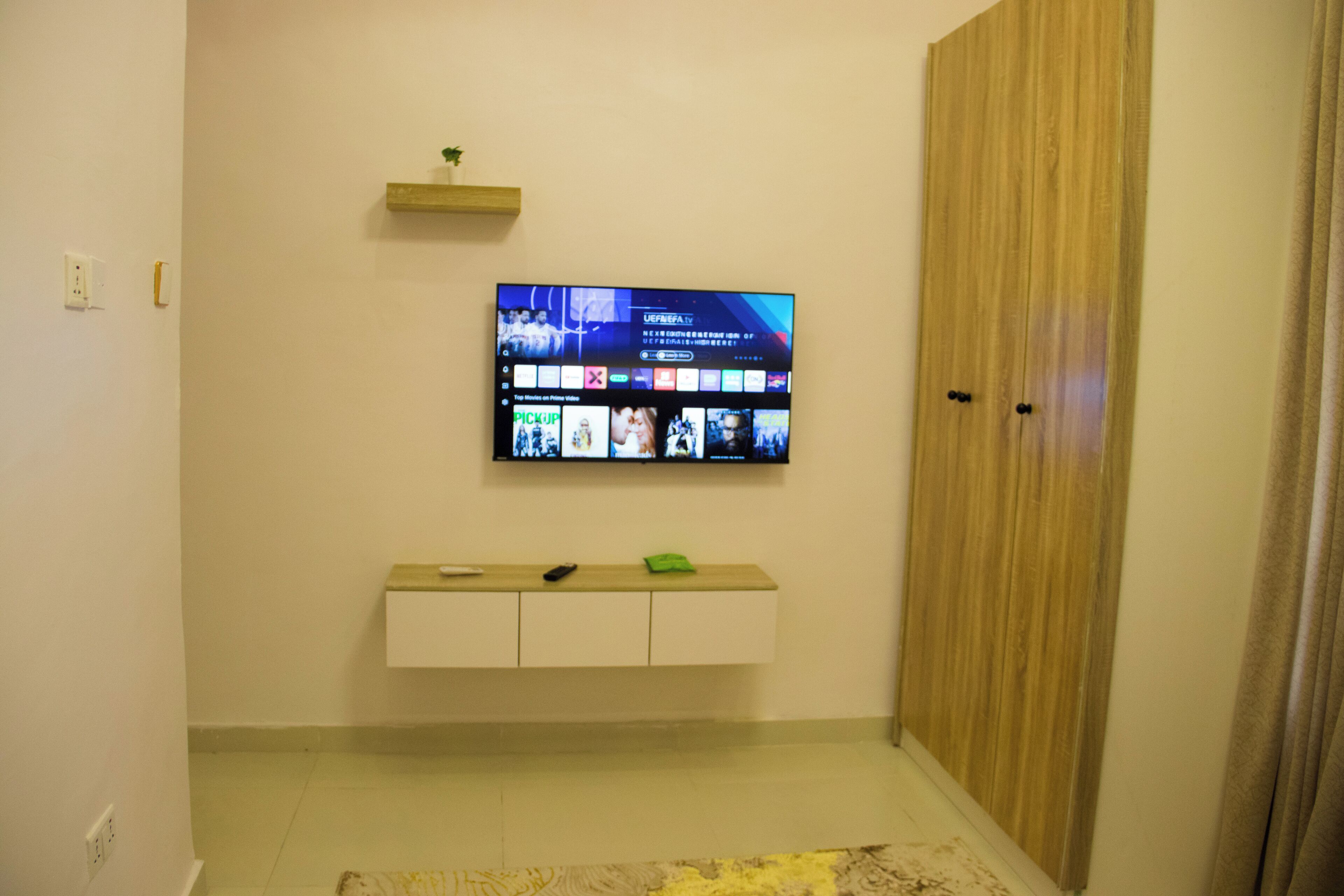 Une pièce avec un téléviseur fixé au mur, un meuble en bois en dessous, et une porte sur la droite.