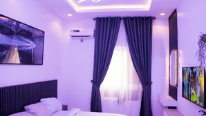 A bedroom with a bed, air conditioning unit, curtains, a TV, and a ceiling light fixture. - AGS Global Homes (Lagos)