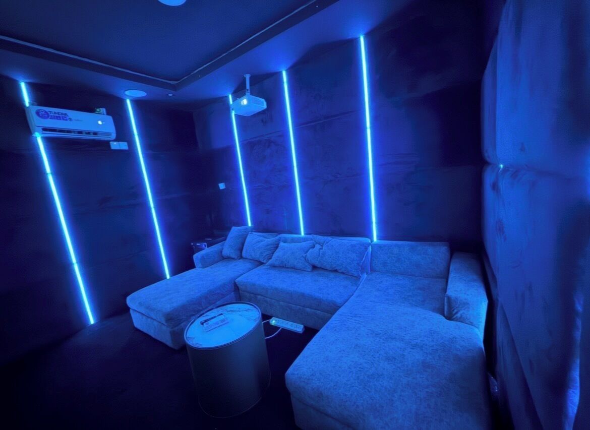 A room with a sectional sofa, a small table, and a trash can.