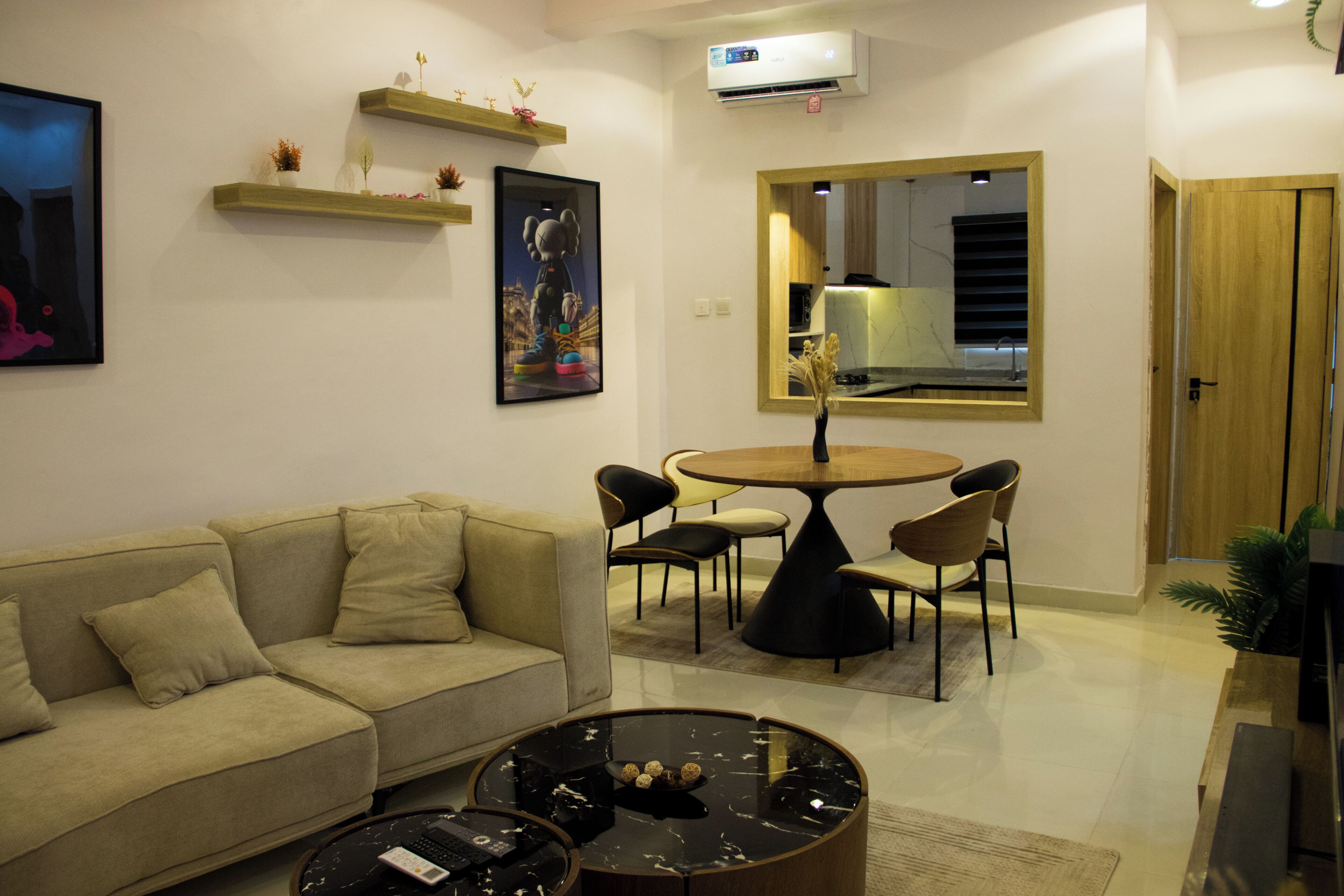 A living room with a sofa, a coffee table, a dining table with chairs, a mirror, and a door.
