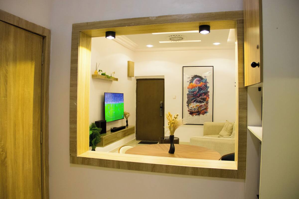 A room with a wooden floor, a flat-screen TV, a sofa, a coffee table, and a mirror.