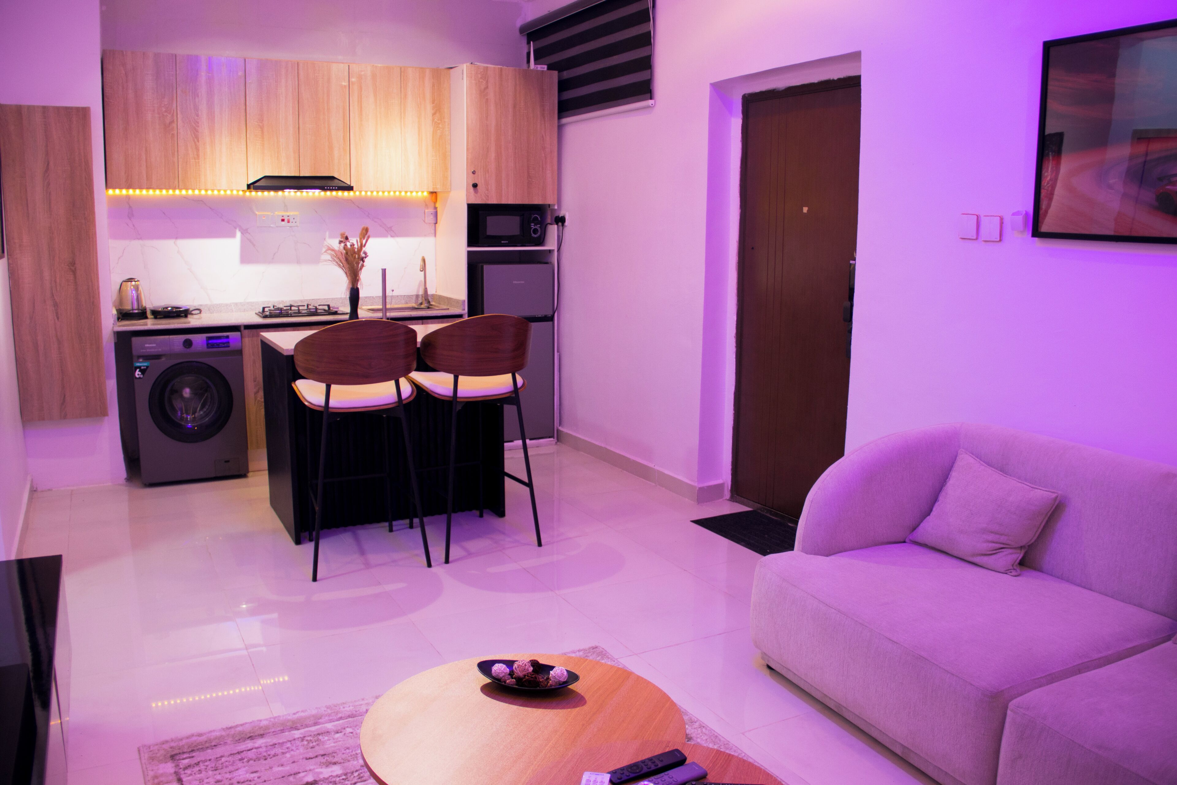 A compact living space with a kitchenette, a sofa, a dining area with chairs, and a washing machine.