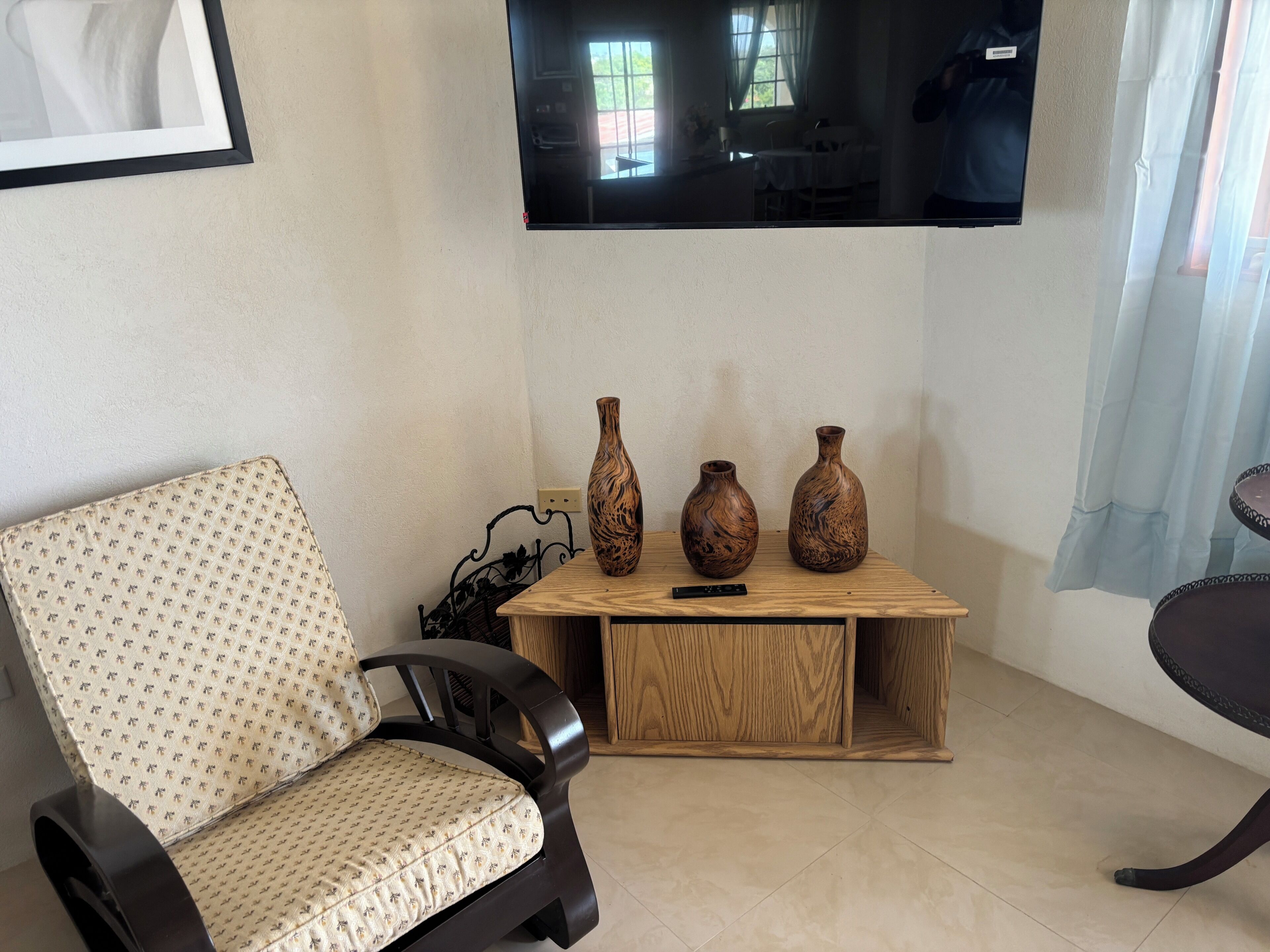 Una sala de estar con un sofá, una mesa de centro de madera con jarrones, un televisor montado en la pared y una silla.