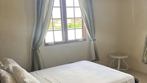 Ein Schlafzimmer mit Bett, Vorhängen, einem Fenster, einer Klimaanlage und einem kleinen Tisch.