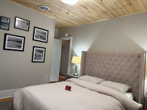 A bedroom with a tufted headboard, a bed with a white comforter, and several framed photographs on the wall.