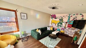 Una sala de estar con un sofá verde, un sillón amarillo, una mesita y un tapete estampado.