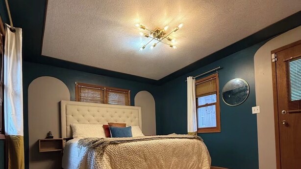 Un dormitorio con una cama, una lámpara en el techo, una ventana con persianas y una puerta.