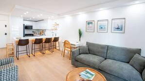 Ein modernes Wohnzimmer mit einem grauen Sofa, einem Couchtisch und einer dahinterliegenden Küchenzeile.