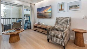 Ein modernes Wohnzimmer mit einem gemusterten Sessel, einem Holztisch und einem Gemälde vom Sonnenuntergang.