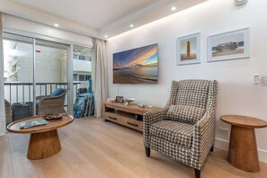 Ein modernes Wohnzimmer mit einem gemusterten Sessel, einem Holztisch und einem Gemälde vom Sonnenuntergang.