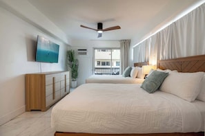Ein Hotelzimmer mit Bett, Fernseher, Deckenventilator, einem Fenster mit Vorhängen und einer Pflanze.