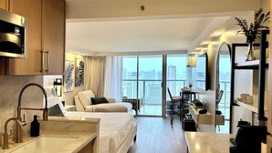 Ein modernes Hotelzimmer mit Küchenzeile, einer Sitzecke, einem Essbereich und einem Balkon mit Blick auf die Stadt.