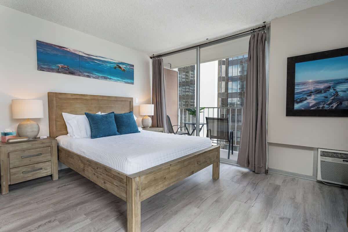 Une chambre d’hôtel moderne avec un lit en bois, une table de chevet, une grande fenêtre avec des rideaux et un balcon offrant une vue.