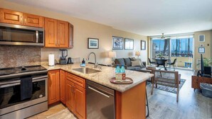 A modern kitchen with granite countertops, wooden cabinets, stainless steel appliances, and a large island with a sink. - Marina Front, Large Lanai, Near Beach (Honolulu)