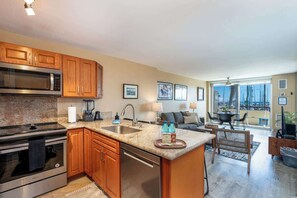 A modern kitchen with granite countertops, wooden cabinets, stainless steel appliances, and a large island with a sink. - Marina Front, Large Lanai, Near Beach (Honolulu)