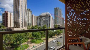 A balcony with a view of tall buildings, a street with cars, and a decorative wooden panel. - Cozy Waikiki Studio, Pool, Gym & BBQ (Honolulu)