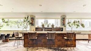 A bar area with a stone counter, wicker bar stools, and a view of the city through large windows. - Cozy Waikiki Studio, Pool, Gym & BBQ (Honolulu)