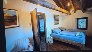Un dormitorio con una cama, una silla, una mesita de noche, un cuadro en la pared y una ventana con vistas.
