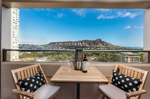 A balcony with a table, two chairs, a bottle of wine, and glasses. A mountain is visible in the background. - Corner Unit, Rare Diamond Head Views, Free Parking (Honolulu)