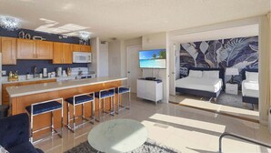 Ein modernes Hotelzimmer mit Küche, Essbereich, Wohnzimmer inklusive Sofa und Fernseher sowie Schlafzimmer mit Bett und Nachttisch.