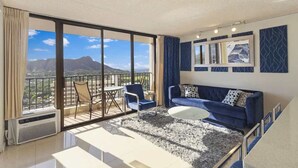 Ein modernes Wohnzimmer mit Balkon, einem blauen Sofa, einem weißen Couchtisch und Blick auf die Berge.