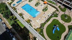 Eine Vogelperspektive eines Hotels mit großem Schwimmbecken, Liegestühlen und einem Spielbereich für Kinder.