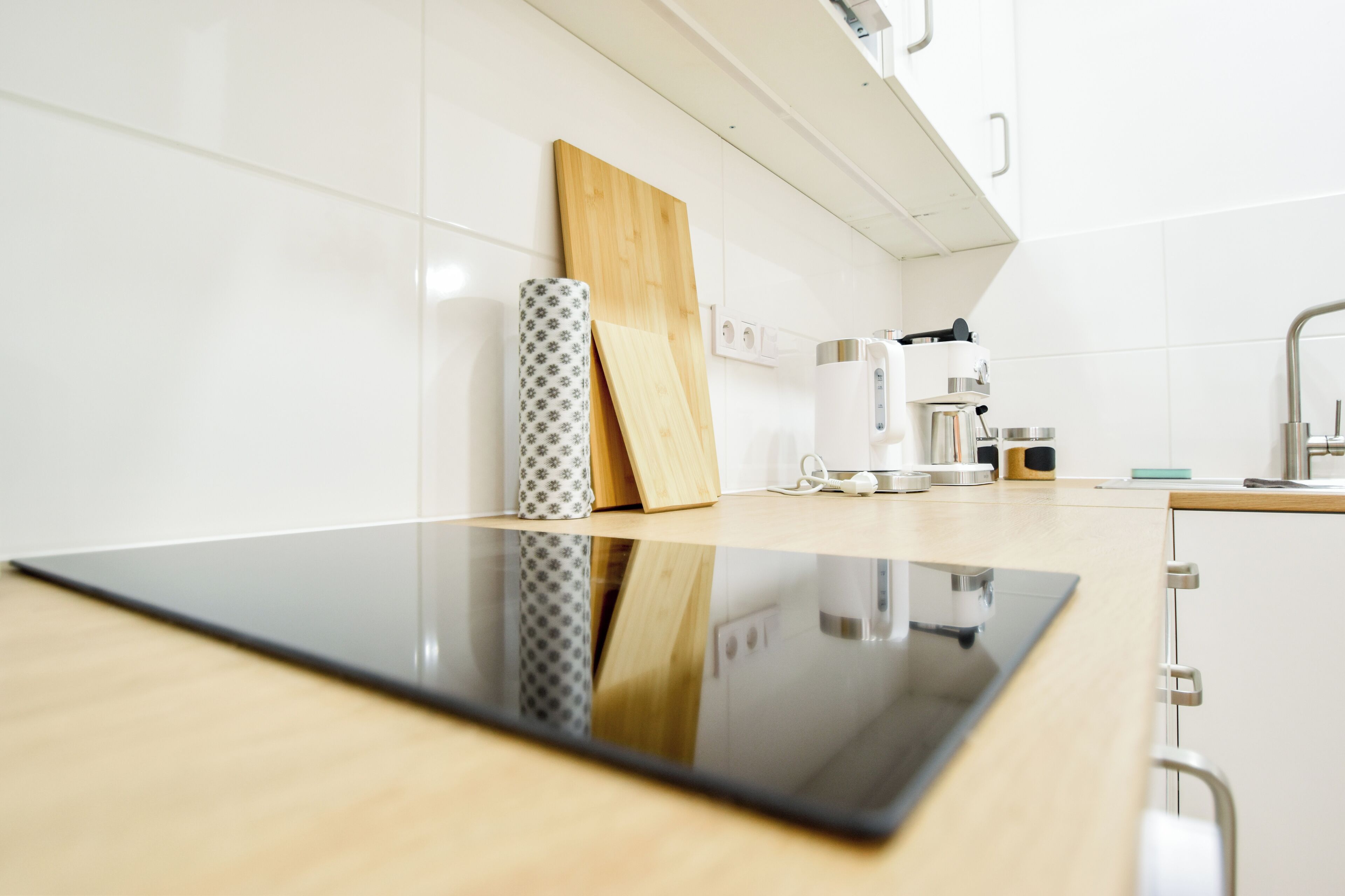 Una cocina moderna con cubierta negra, tabla de cortar de madera, florero estampado y cafetera.