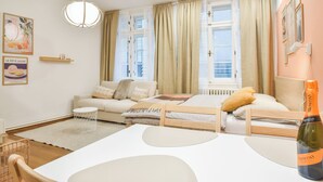 A modern hotel room with a wooden bed, a white table, a bottle of wine, a sofa, and a view of the city. - Enjoyable 1-bedroom apartment in charming Olomouc city center (Olomouc)