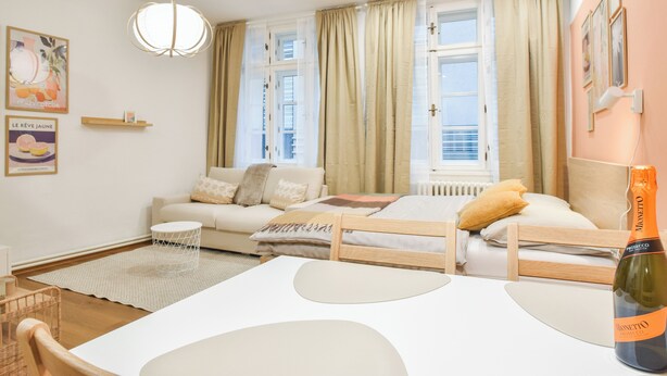 Una habitación de hotel moderna con una cama de madera, una mesa blanca, una botella de vino, un sofá y vistas a la ciudad.