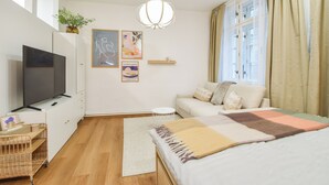 A modern bedroom with a bed, a television, a small side table, a sofa, and a window with curtains. - Enjoyable 1-bedroom apartment in charming Olomouc city center (Olomouc)
