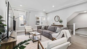 Ein modernes Wohnzimmer mit einer Couch, Sesseln, einem Couchtisch und einem Fernseher.