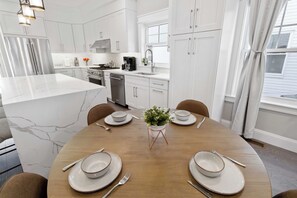 A modern kitchen with white cabinetry, a central island with a marble countertop, and a dining area set for four with white plates and silverware.