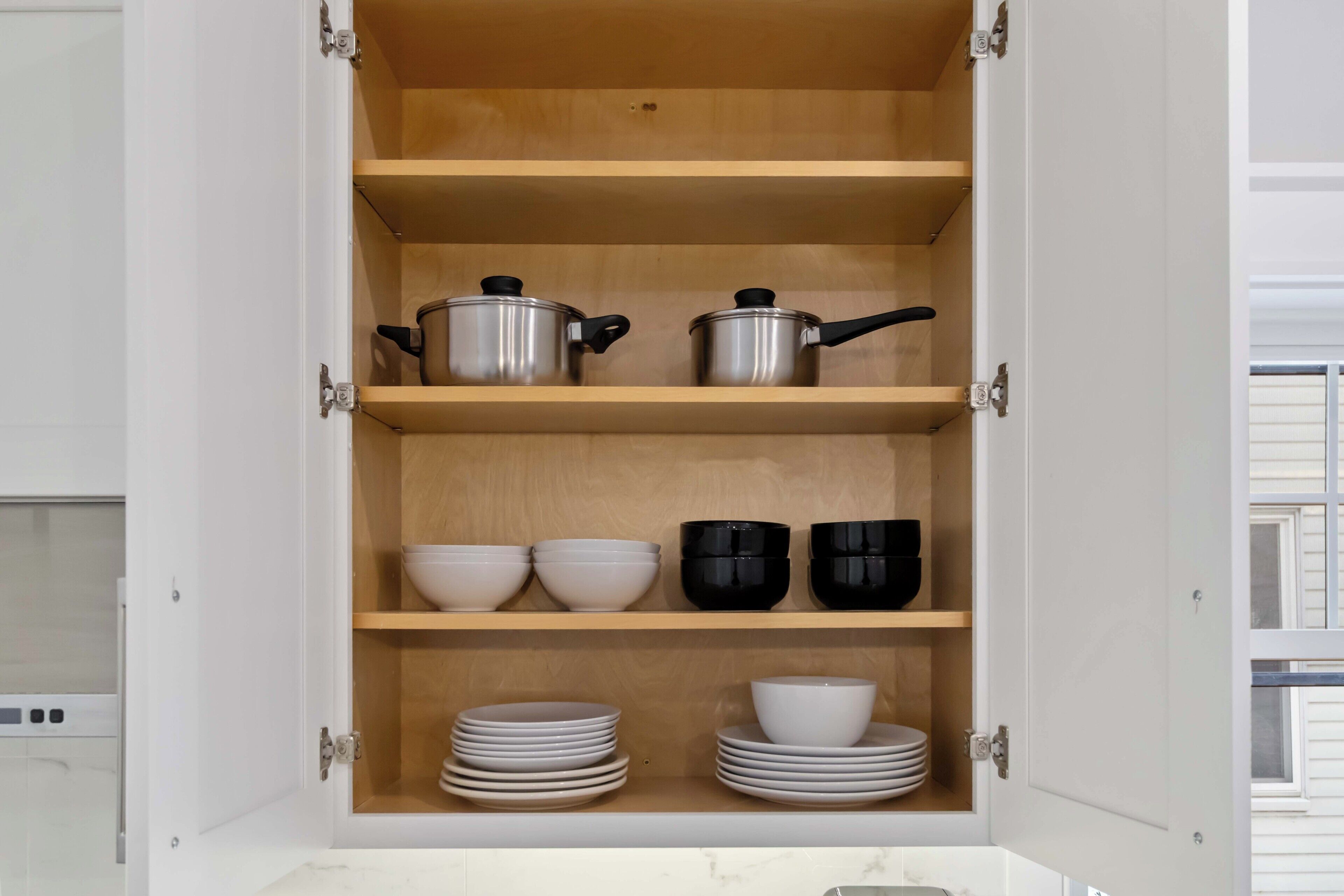A kitchen cabinet with shelves, pots, bowls, and stacked plates.