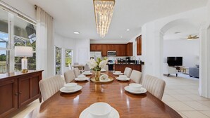 Un comedor amplio con una gran mesa de madera, vajilla blanca y una araña.