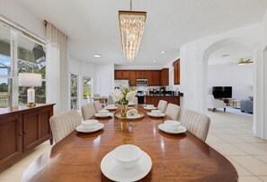 A spacious dining area with a large wooden table, white dinnerware, and a chandelier. - NEW | Free Pool Heat | Gameroom | Sunset View | Minutes from Disney (Kissimmee)