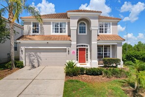 A two-story house with a red door, a garage, and a well-maintained lawn. - NEW | Free Pool Heat | Gameroom | Sunset View | Minutes from Disney (Kissimmee)