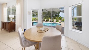 Un comedor con una mesa redonda, sillas, un armario de madera y vistas a una piscina a través de puertas de vidrio grandes.