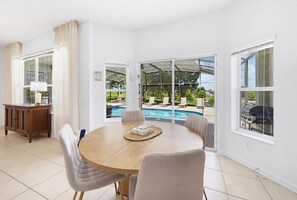 A dining area with a round table, chairs, a wooden cabinet, and a view of a swimming pool through large glass doors. - NEW | Free Pool Heat | Gameroom | Sunset View | Minutes from Disney (Kissimmee)