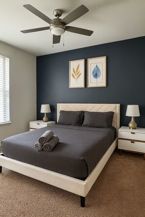 Une chambre à coucher comprenant un lit, deux tables de chevet, un ventilateur de plafond et deux œuvres d’art murales.