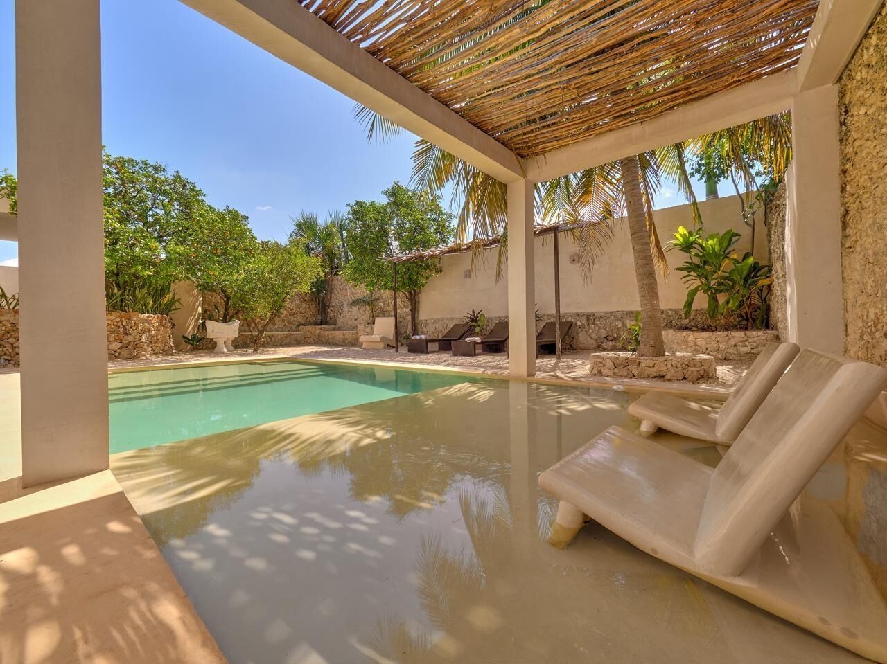 A pool area with lounge chairs, a pergola, and surrounding greenery.
