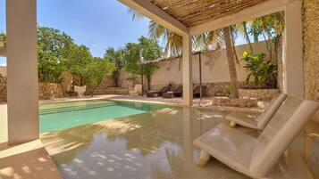 A pool area with lounge chairs, a pergola, and surrounding greenery.